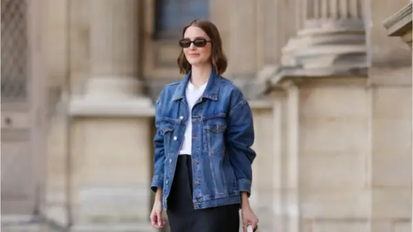 Donna con occhiali da sole indossa un outfit giacca jeans donna, t-shirt bianca e gonna nera.