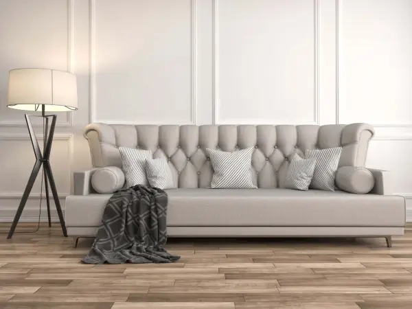 Divano imbottito grigio con cuscini a righe e coperta geometrica. La luce soffusa di una lampada da terra illumina la scena, dimostrando come grigio e beige stiano bene insieme.